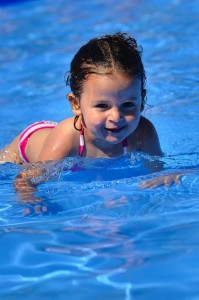 Petite fille en train de nager dans la piscine en plein soleil