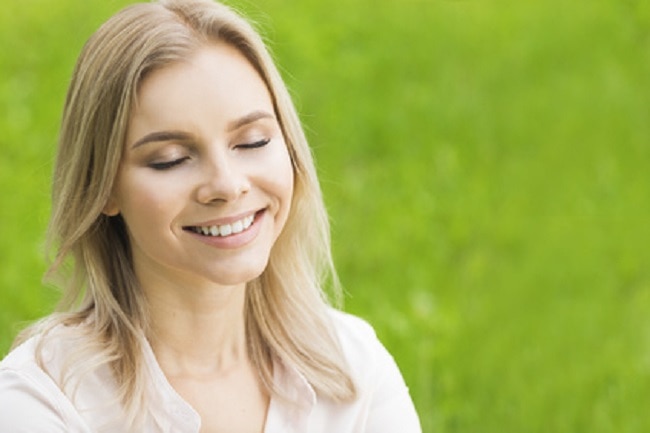 Jeune femme blonde souriante yeux fermés sur fond d'herbe