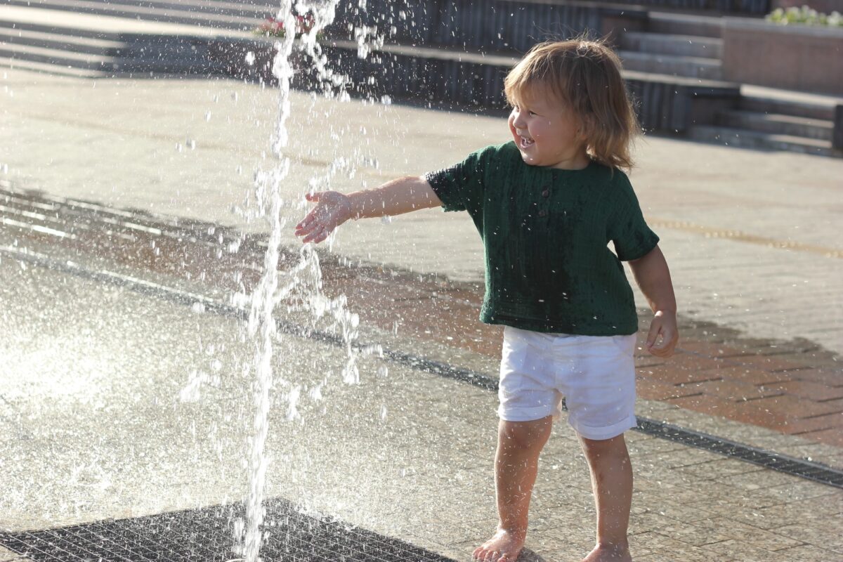 Jeune enfant jouant avec une fontaine dans la rue, symbole des espaces publics pensés pour les familles