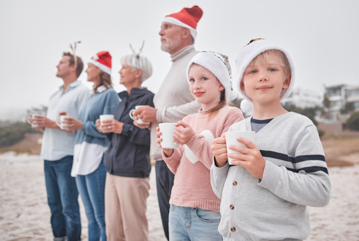 famille intergenerationnelle sur la plage en hiver avec bonnets de père noel et mug chocolat chaud