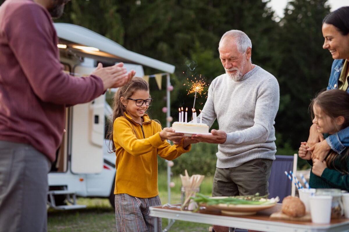 petite fille apporte un gateau d'anniversaire a son grand-pere lors de vacances en camping