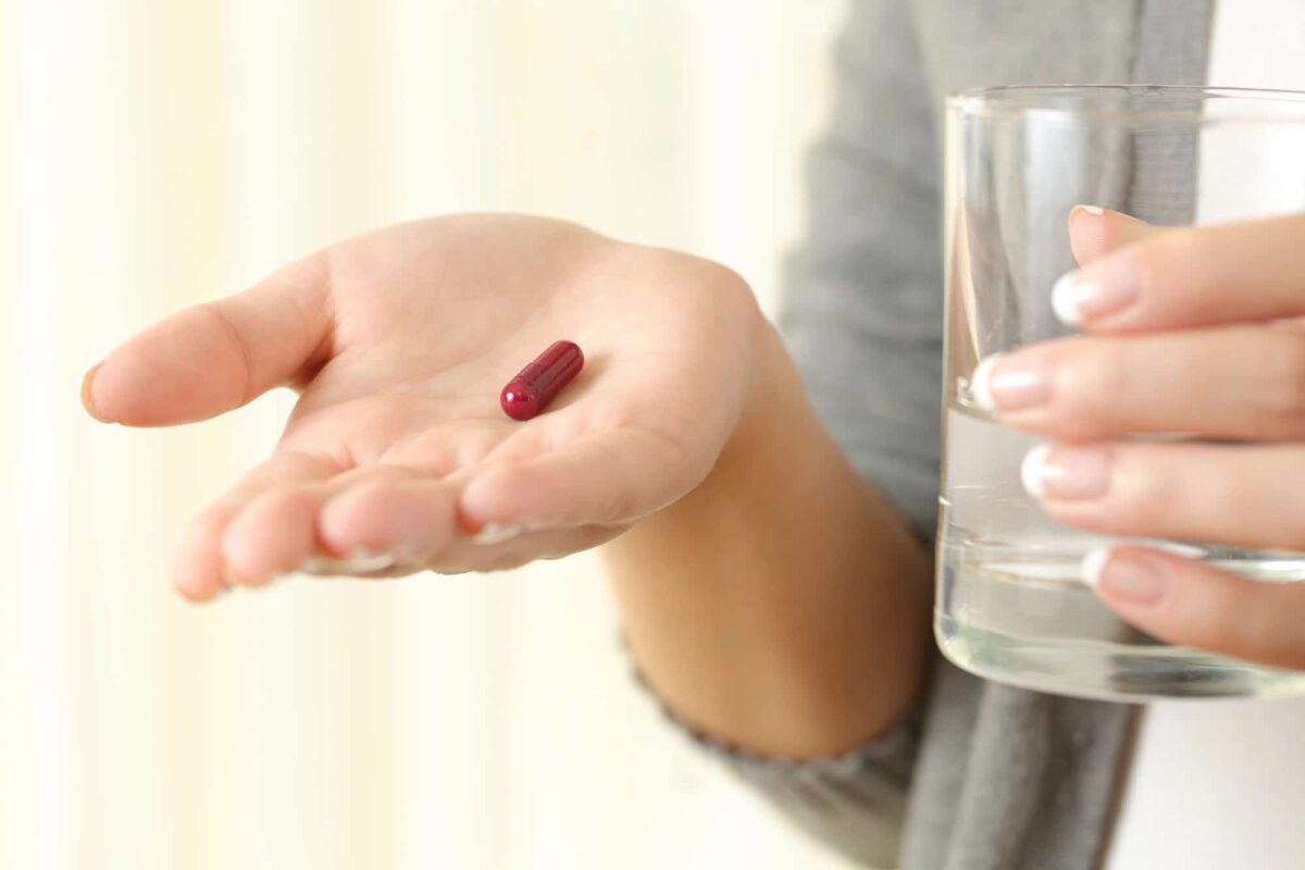 femme prenant un complément alimentaire avec un verre d'eau contre les effets de la ménopause