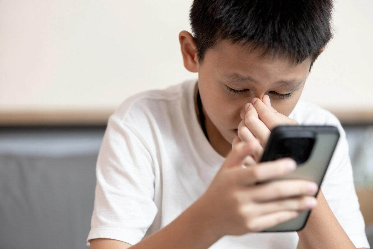 jeune garçon sur son téléphone souffrant de fatigue occulaire